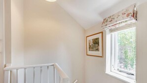 Eine Treppe mit weißer Handläufung, ein gerahmtes Bild an der Wand und ein Fenster mit blumigem Vorhang.