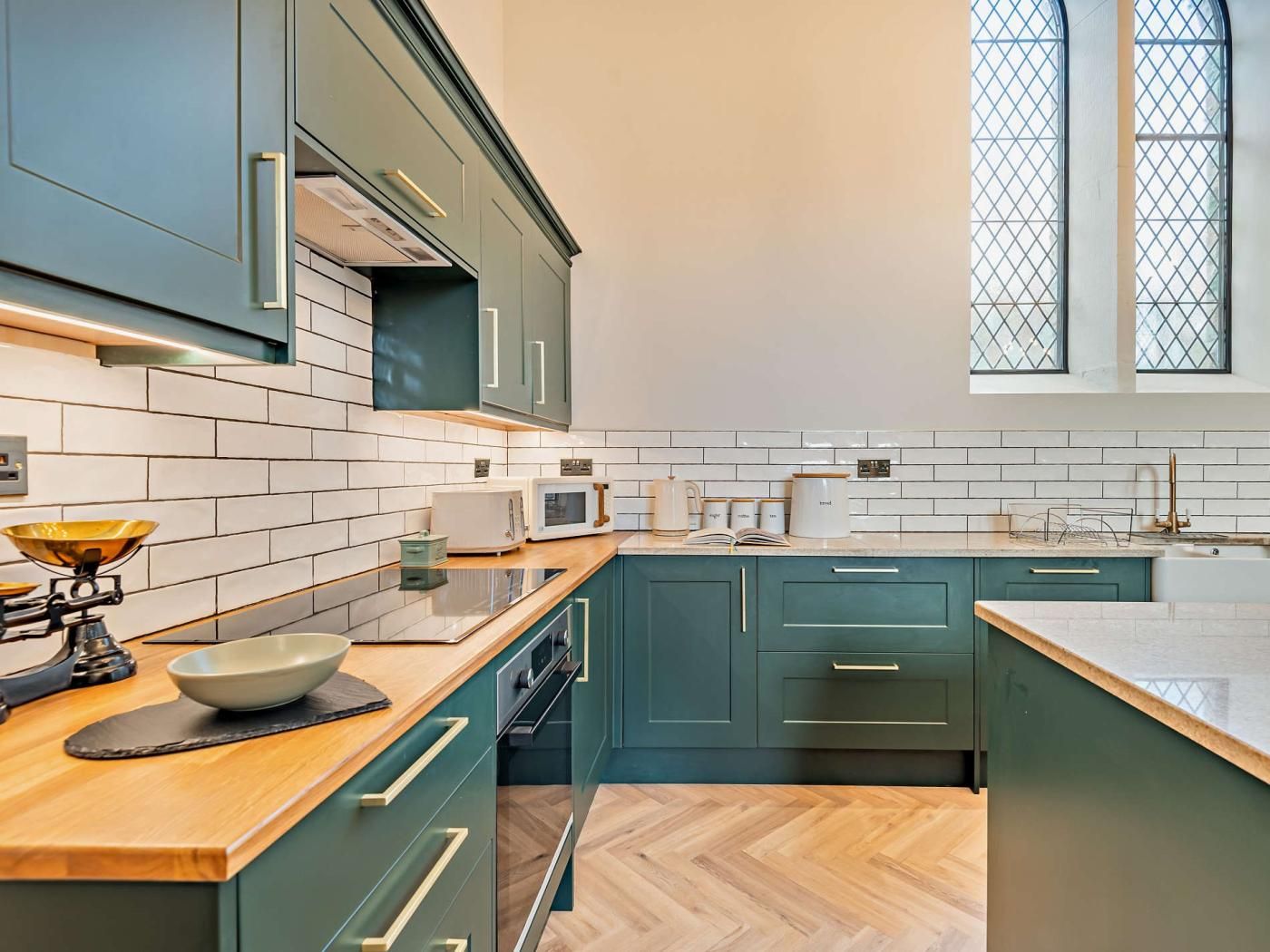 Une cuisine moderne avec des meubles de couleur turquoise, des carreaux de céramique blancs disposés en motif métro et un plan de travail en bois.