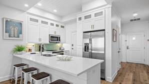 Una cocina moderna con armarios blancos, electrodomésticos de acero inoxidable, una isla grande con taburetes y un salpicadero con azulejos verdes.