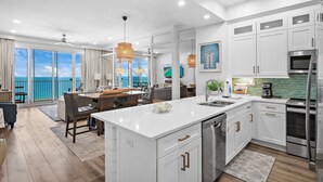 Cocina moderna con armarios blancos, una isla central, electrodomésticos de acero inoxidable y vista al océano.