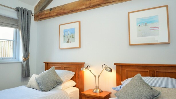 Ein Schlafzimmer mit zwei Betten, Holzbalken, einem Nachttisch mit Lampe und zwei gerahmten Bildern an der Wand.