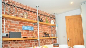 Eine Küche mit Backsteinwänden, Holzregalen und einem Schild mit der Aufschrift 'Sandy Toes & Salty Kisses', sowie einem Teller mit Gebäck.
