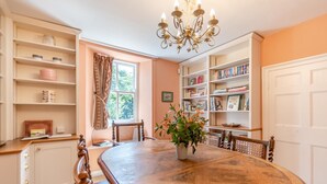 Ein Essbereich mit einem Holztisch, Stühlen, einer Chandelüster und einer Bücherwand voller Bücher.