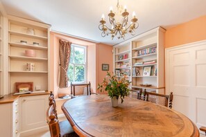 A dining area with a wooden table, chairs, a chandelier, and a bookshelf filled with books. - 3 Bed in Castlemorris (oc-94522) (Castlemorris)