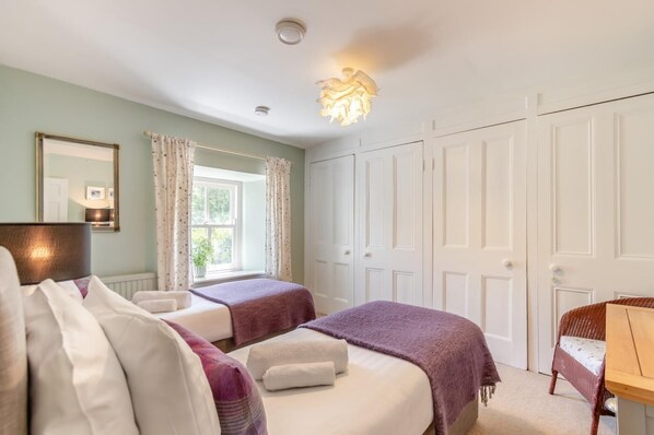 A hotel room with two beds, a sitting area, a window with curtains, a mirror, and a wardrobe. - 3 Bed in Castlemorris (oc-94522) (Castlemorris)