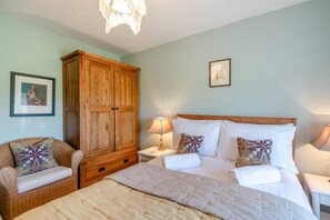 A bedroom with a large bed, a wooden wardrobe, a nightstand with a lamp, and a framed picture on the wall. - 3 Bed in Castlemorris (oc-94522) (Castlemorris)