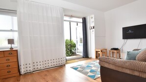 Uma sala de estar com sofá, televisão, piso de madeira e uma janela com cortinas.