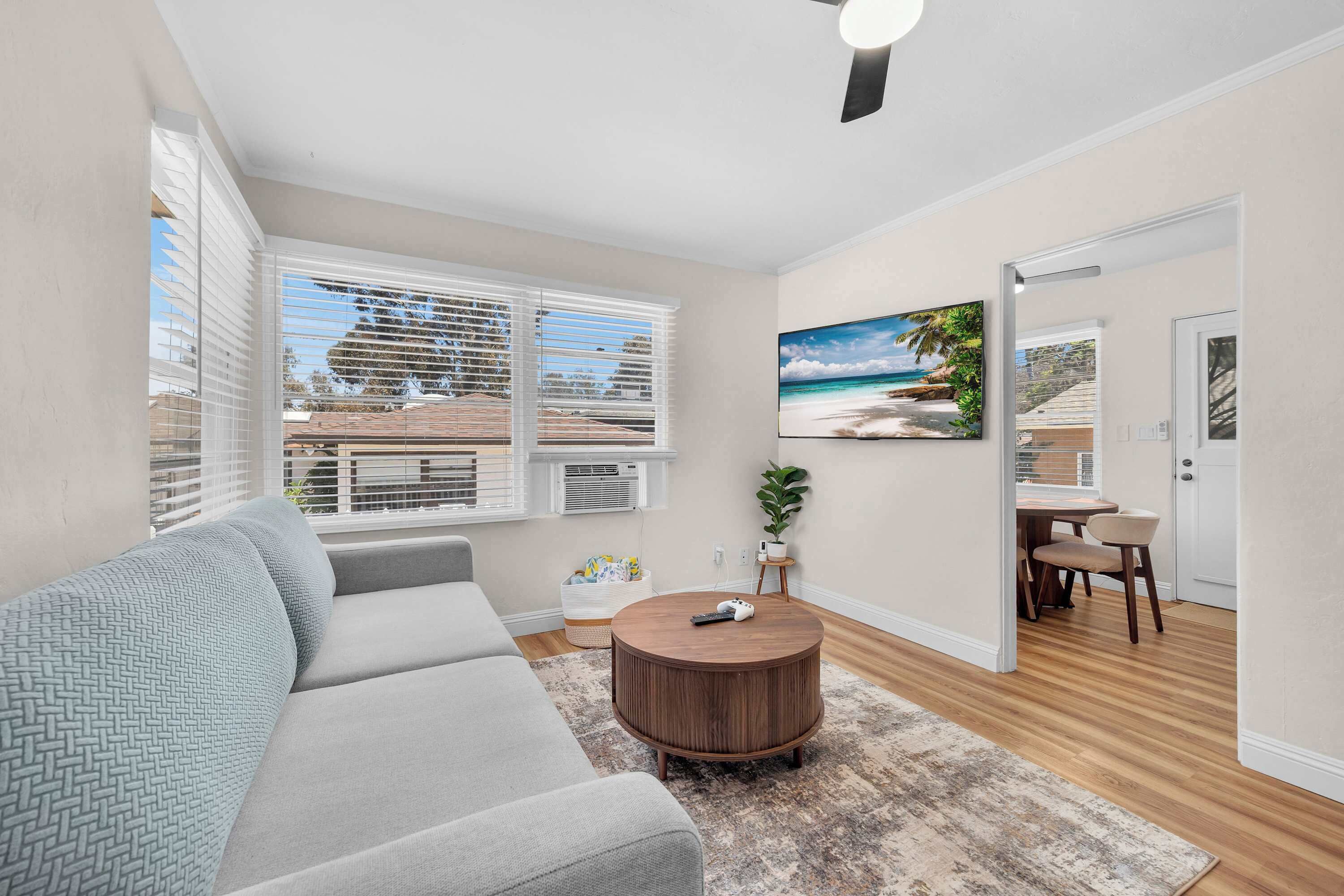 A living room with a sofa, a round coffee table, a painting, and a dining area with chairs and a table.