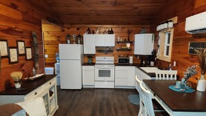 Cocina compacta con electrodomésticos blancos, paredes de madera y un comedor con mesa y sillas blancas.