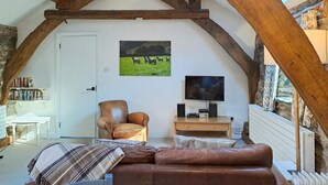 Una camera in stile loft con travi a vista in legno, un comodo divano in pelle, una televisione e una libreria.