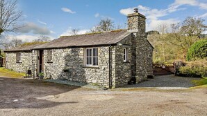 Une petite maison en pierre avec une cheminée, un petit porche et une allée gravillonnée.