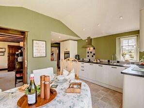 A modern kitchen with white cabinets, a wooden dining table set with plates, a wine bottle, and salt and pepper shakers. - 1 Bed in Ulverston (oc-91660) (Satterthwaite)