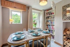 A dining area with a table set for four, a bookshelf, and a window with curtains. - 3 Bed in Lydbrook (oc-94490) (Central Lydbrook)
