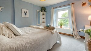 Et soveværelse med en stor seng, et sengebord, et vindue med gardiner og en hængende lampe.