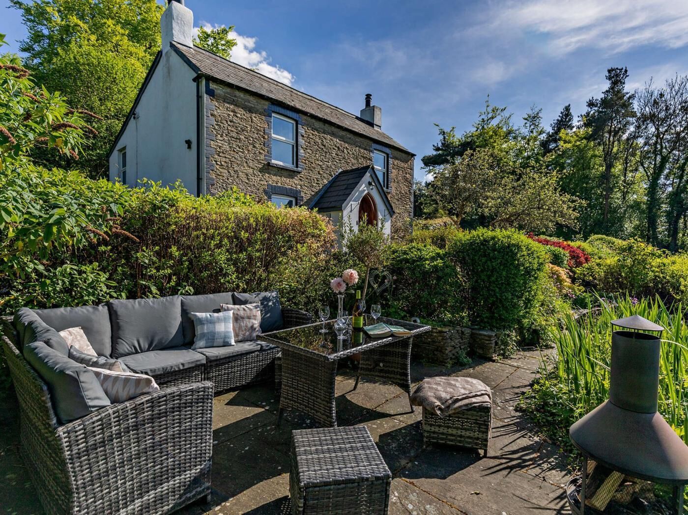 A stone house with a garden patio featuring wicker furniture and a table with wine glasses.