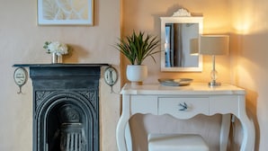 Et værelse med en pejs, et hvidt konsolbord med et spejl og en lampe, samt en pyntende plante.
