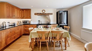 Una cocina con armarios de madera, una mesa de comedor con sillas, un refrigerador y un reloj en la pared.