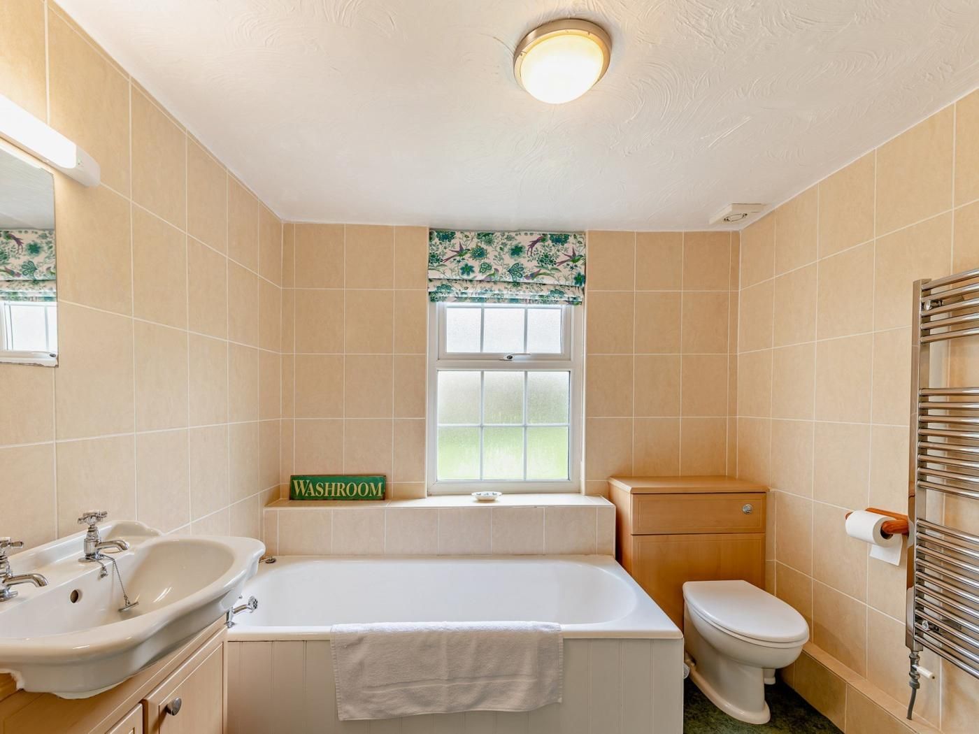 A bathroom with a sink, bathtub, toilet, and a window with a 'WASHROOM' sign.