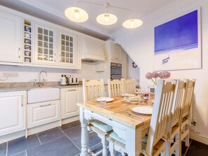 A kitchen with white cabinets, a wooden dining table, and a blue painting on the wall. - 3 Bed in Bideford (oc-57804) (Appledore)