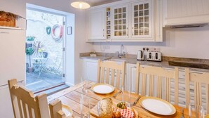 A kitchen with white cabinets, a dining table set for two, and a view into the garden. - 3 Bed in Bideford (oc-57804) (Appledore)