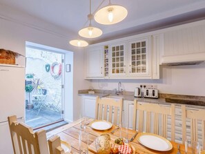 A kitchen with white cabinets, a dining table set for two, and a view into the garden. - 3 Bed in Bideford (oc-57804) (Appledore)