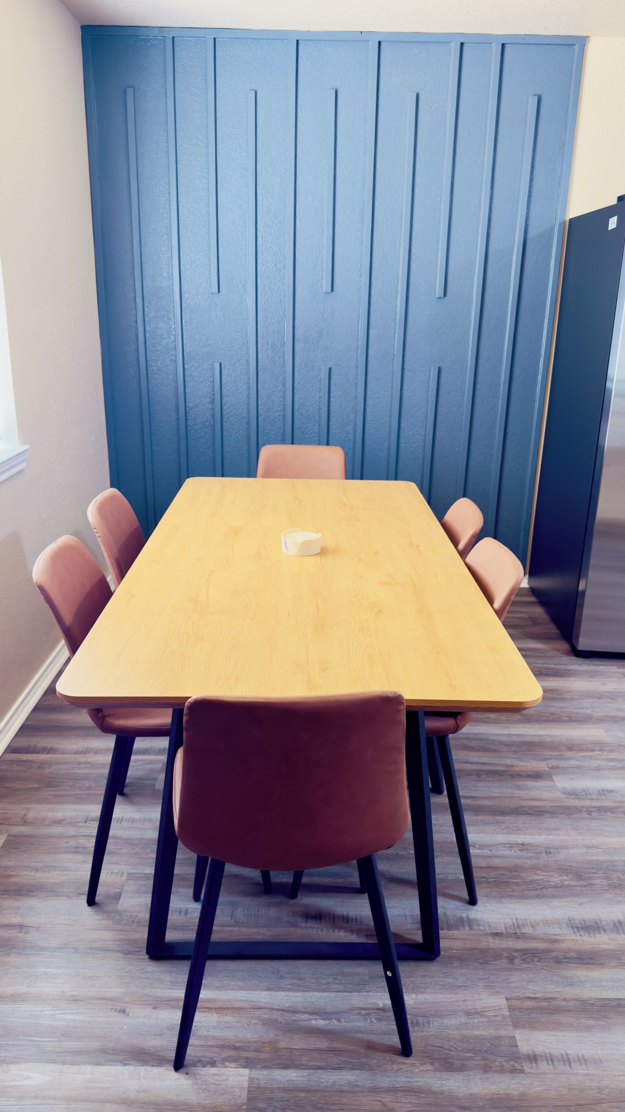 Ein Konferenzraum mit einem Holztisch, sechs Stühlen, einer blauen Akzentwand und einem Kühlschrank.