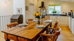 Een eethoek met een houten tafel voor vier personen, omringd door stoelen, en een vaas met gele bloemen op de tafel.