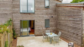 Een houten huis met een terras, een schuifpui en een tafel met stoelen.