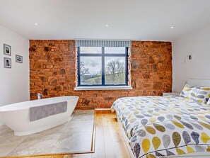 Ein modernes Badezimmer mit einer freistehenden Badewanne, einem großen Fenster mit Blick auf Bäume und einem Bett mit einem gemusterten Duvet.