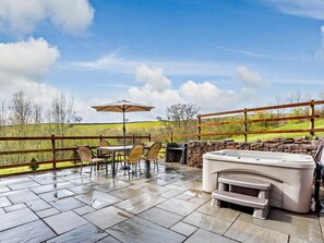 Eine Terrasse im Freien mit Steinboden, einem Tisch mit Stühlen, einem Grill und einem Whirlpool.