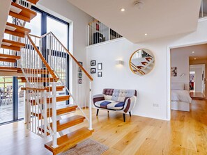 Ein modernes Interieur mit einer Holztreppe, einem runden Spiegel und einem gemusterten Sofa.