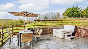 Een terras buiten met een tafel, stoelen, een barbecue en een stenen muur.