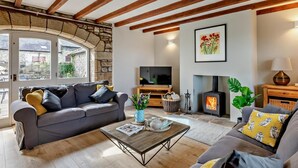 A cozy living room with a stone wall, wooden beams, a fireplace, and a television. - 3 Bed in Alnwick (oc-94195) (Christon Bank)