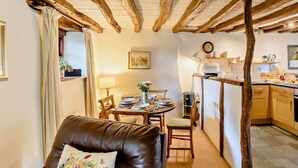 Una habitación acogedora con vigas de madera a la vista, un comedor con mesa para dos personas y una kitchenette equipada con electrodomésticos modernos.