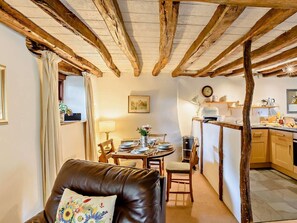Ein gemütliches Zimmer mit freiliegenden Holzbalken, einer Essecke mit Tisch für zwei Personen und einer Küchenzeile mit modernen Geräten.