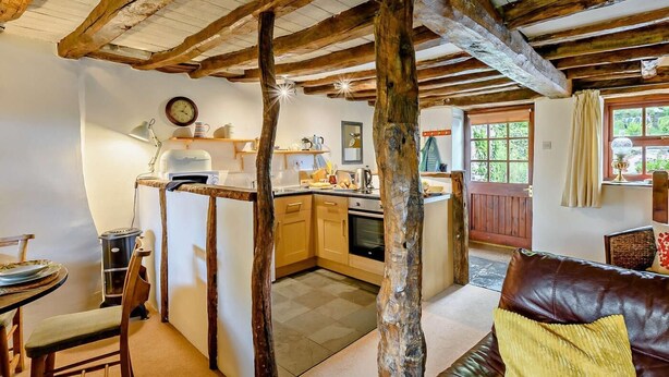 Una cocina rústica con vigas de madera, un comedor con mesa y sillas, y una sala de estar con sofá de cuero.