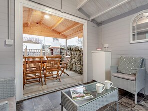 Un patio techado con mobiliario de madera, una mesa de vidrio con revistas y una pared de piedra.