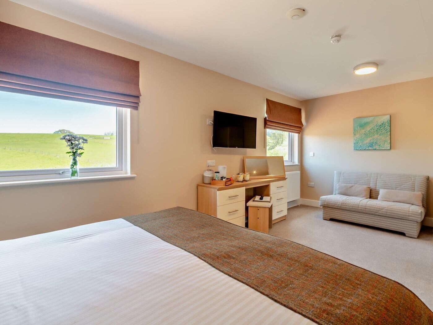 Ein Schlafzimmer mit Bett, Schreibtisch, Fernseher, Sofa und einem Fenster mit Blick auf ein Feld.