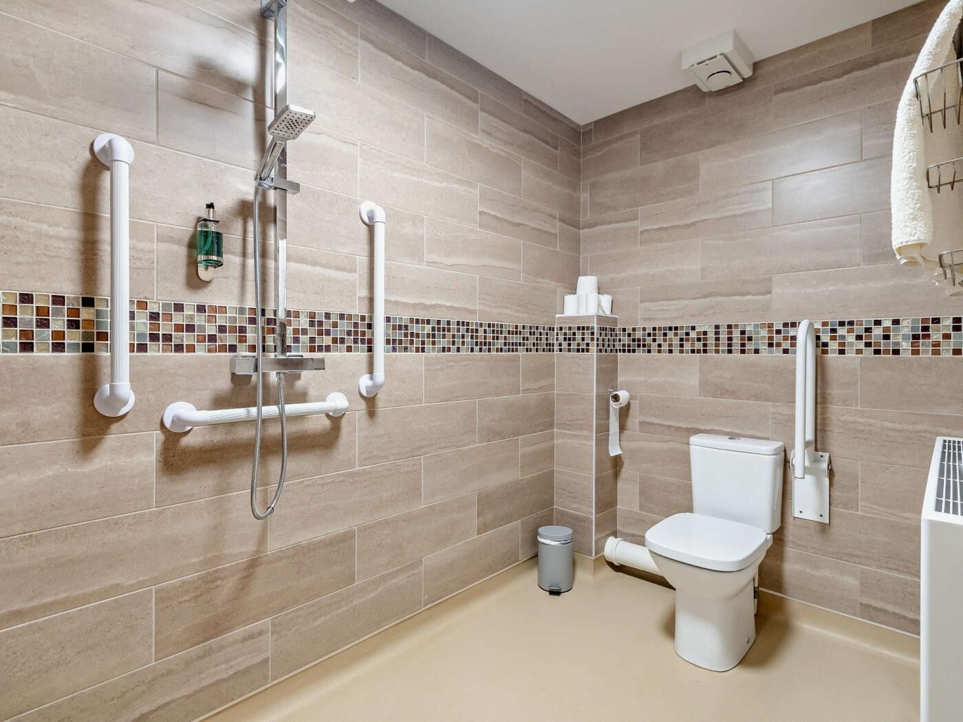 A bathroom with a shower, toilet, and grab bars.