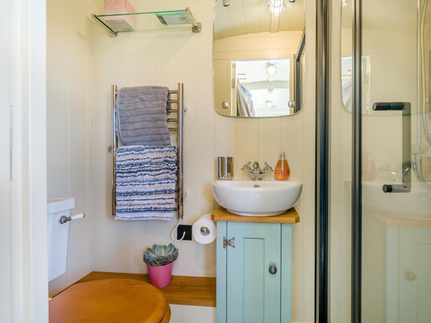 Un bagno con il water, un lavandino, uno specchio, un porta asciugamani e uno spazio doccia.