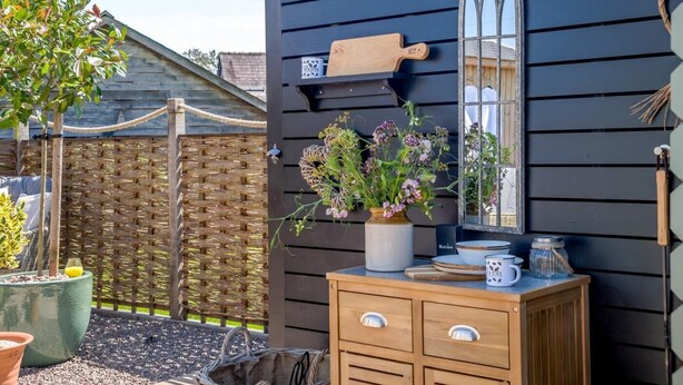 A wooden outdoor kitchen area with a built-in stove, a hanging pot rack, and a potted plant. - 1 Bed in Leominster (oc-93060) (Pembridge)