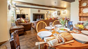 Un coin repas avec une table en bois dressée pour le repas, une cheminée et un salon avec un canapé et un téléviseur.