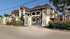 A large, two-story house with a gated entrance, multiple windows, and a prominent front door. - Relax in luxury and sleep in peace. (Discovery Bay)