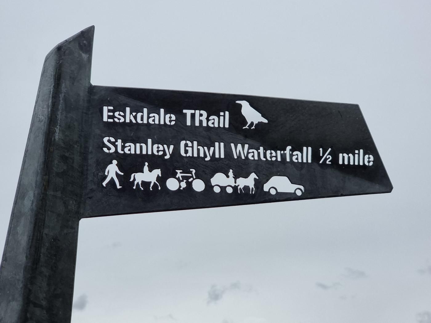 Indicador direccional del sender Eskdale Trail i la cascada Stanley Ghyll, que indica que el sender es troba a mig millar de milles.