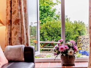 A room with a view of a garden through a glass door, a wooden table with a vase of flowers, and a sofa. - 1 Bed in Holmrook (oc-94530) (Eskdale)