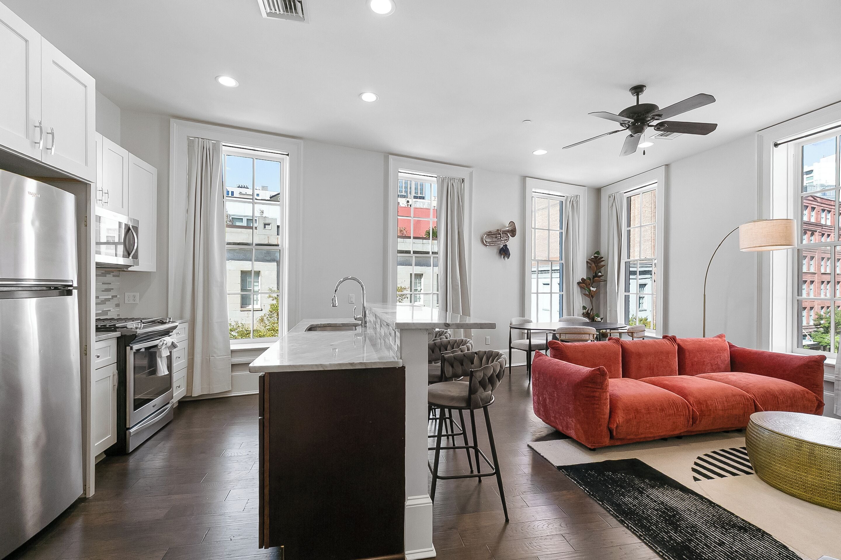 Una cocina moderna con una isla central, taburetes de bar y un sofá rojo.