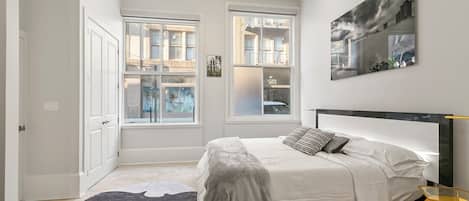 A bedroom with a bed, a ceiling fan, two windows, and a rug.