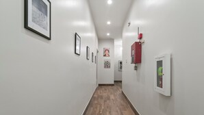 A hallway with framed pictures on the walls, a fire alarm, and a thermostat. - The Melody  (New Orleans)