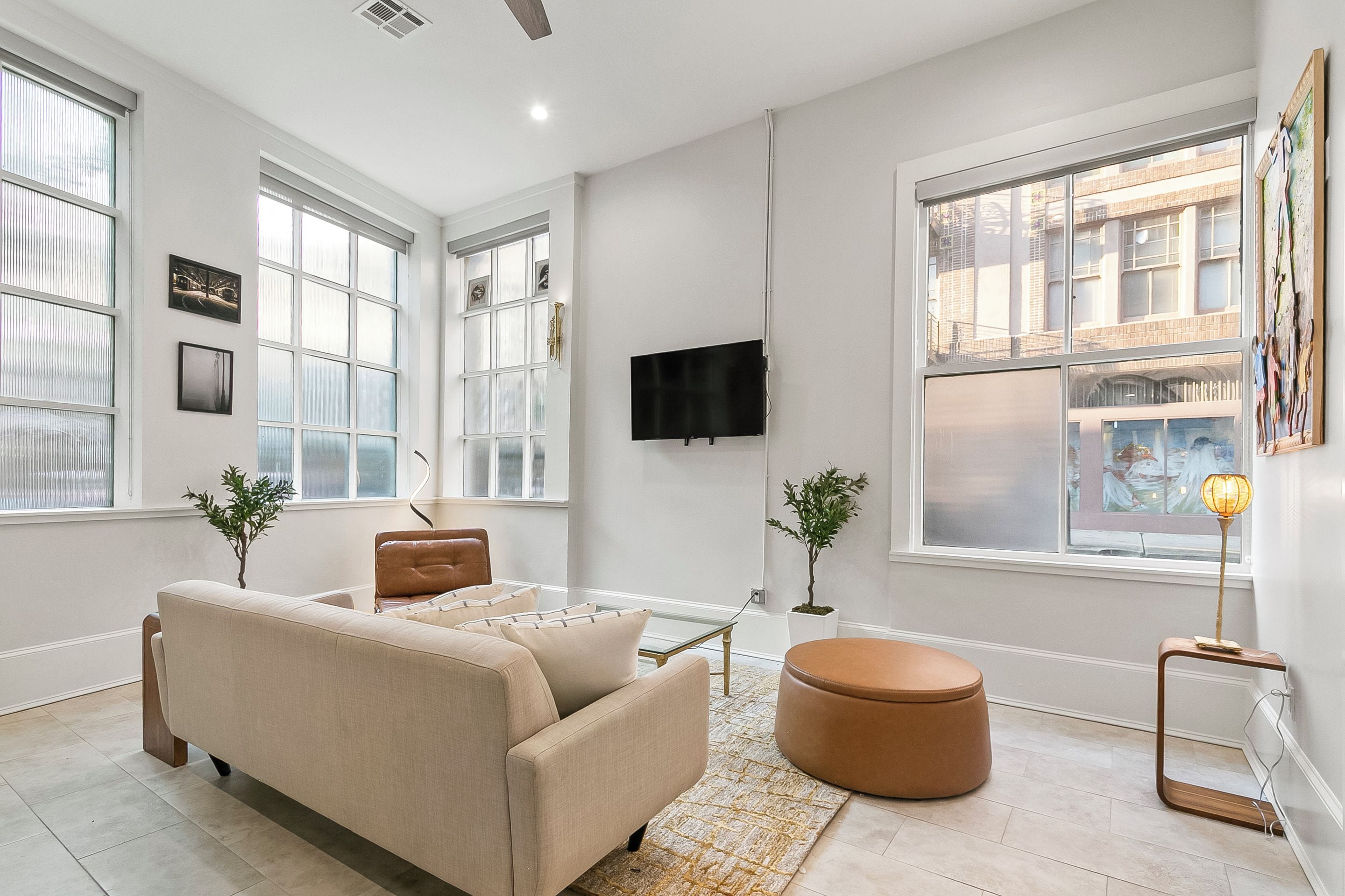 A modern living room with a sofa, ottoman, and a flat-screen TV mounted on the wall.