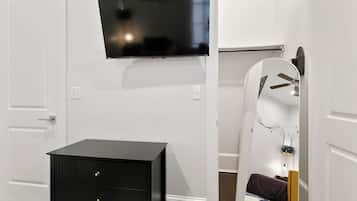 Quarto com televisão de tela plana na parede, cômoda preta com gavetas e um espelho grande com moldura decorativa.